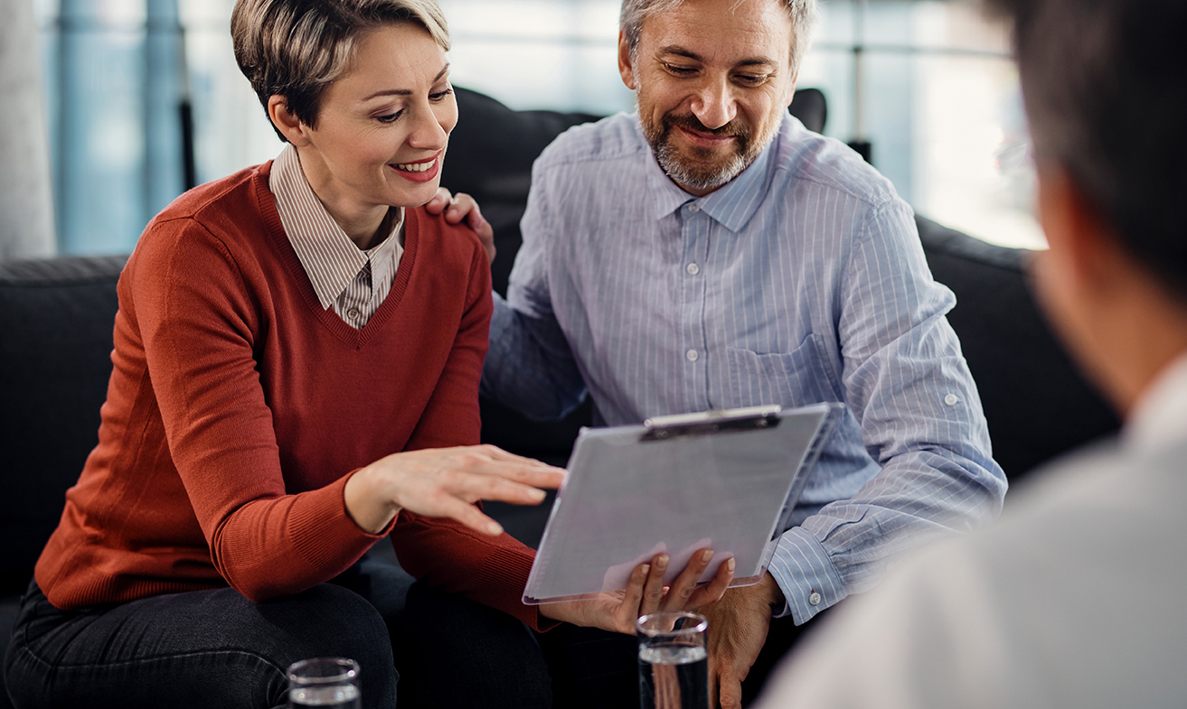 Happy couple analyzing documents while having a meeting with insurance agent in the office.