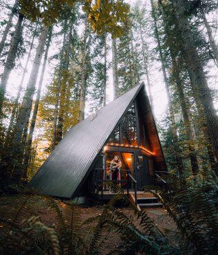A-frame cabin in the woods surrounded by tall evergreen trees.