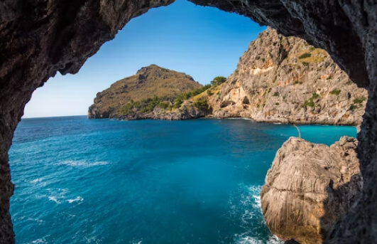 VIew of ocean blue water and craggly rock from inside of a dark cave.