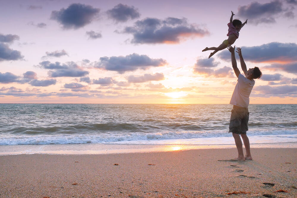 Father and daughter playing on beach in front of sunrise